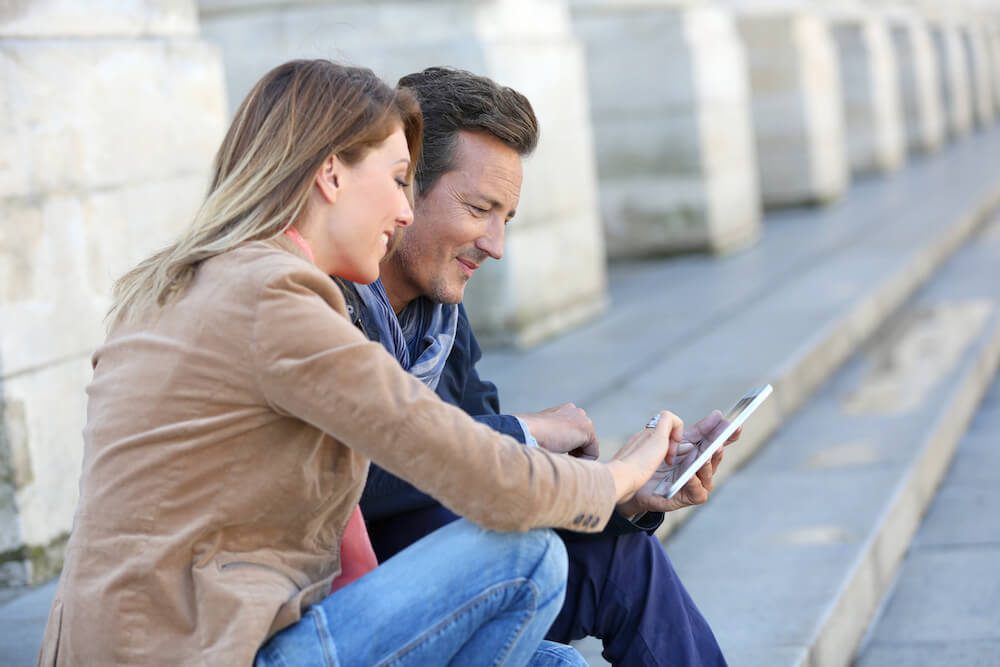 A couple sitting outdoor attending a remote audiology appointment on mobile