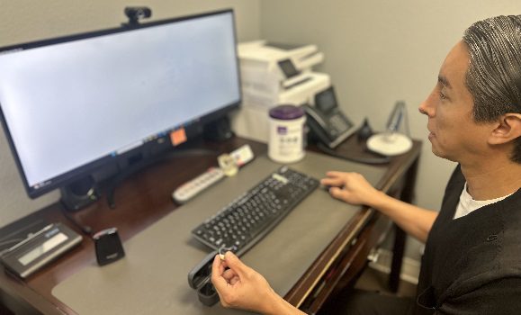 danny_garcia_at_his_desk_and_holding_a_hearing_aid_img
